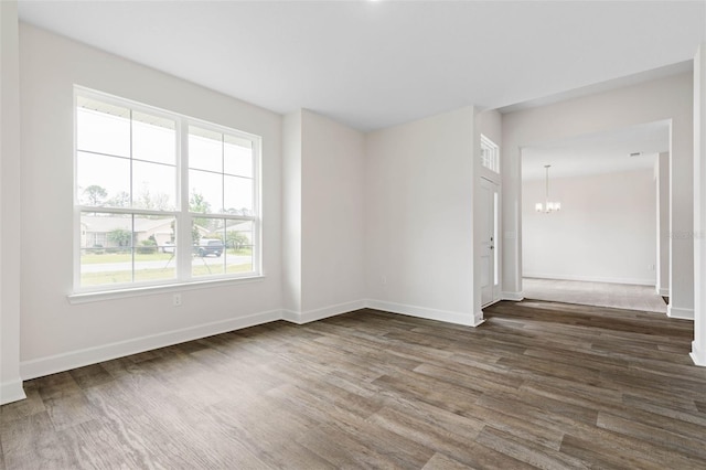 spare room with baseboards, a notable chandelier, and dark wood finished floors