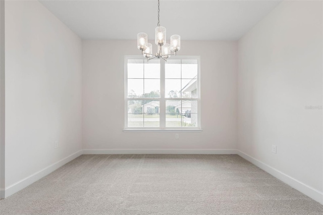 spare room with an inviting chandelier, light colored carpet, and baseboards