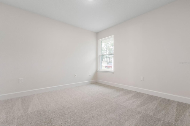 spare room featuring light colored carpet and baseboards