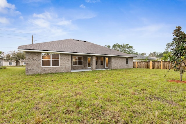 back of property with brick siding, roof with shingles, a yard, and fence