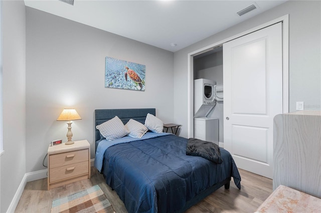 bedroom featuring hardwood / wood-style flooring, stacked washing maching and dryer, and a closet