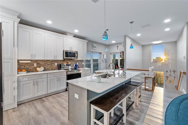 kitchen with a kitchen breakfast bar, stainless steel appliances, a kitchen island with sink, pendant lighting, and white cabinets