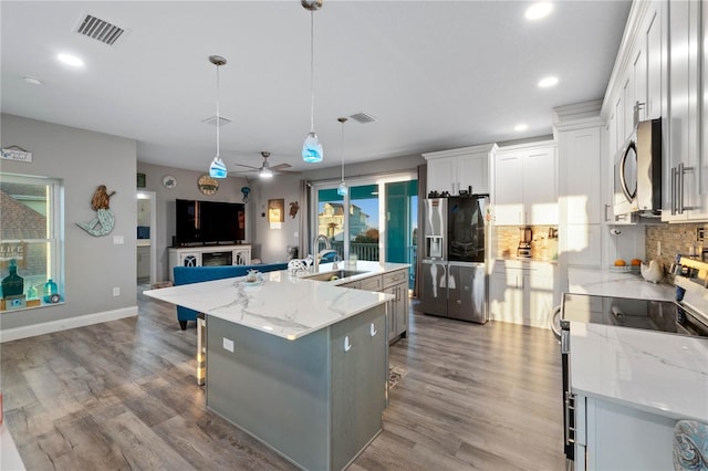 kitchen with appliances with stainless steel finishes, sink, white cabinetry, hanging light fixtures, and a large island