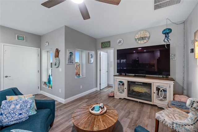 living room with ceiling fan, wood-type flooring, and a fireplace