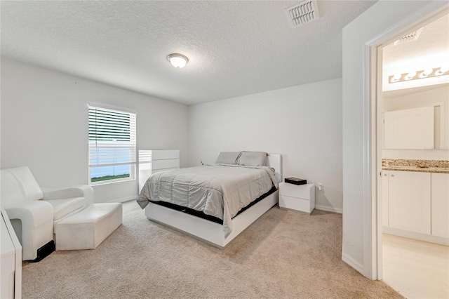 carpeted bedroom featuring ensuite bathroom and a textured ceiling