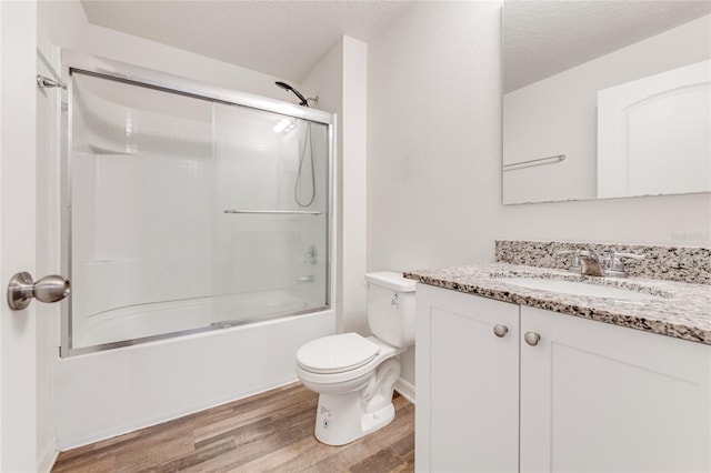 full bathroom with vanity, a textured ceiling, shower / bath combination with glass door, hardwood / wood-style flooring, and toilet