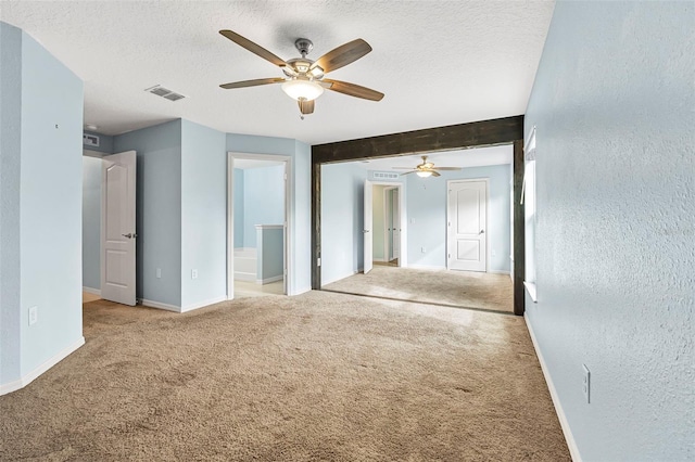 carpeted empty room with ceiling fan, beamed ceiling, and a textured ceiling