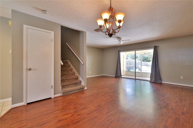 empty room with a textured ceiling, dark wood-type flooring, and ceiling fan with notable chandelier