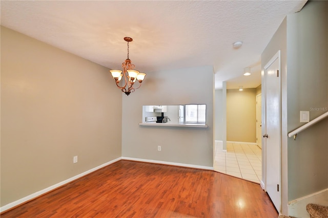 empty room with an inviting chandelier, a textured ceiling, and light wood-type flooring