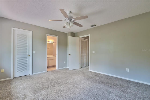 unfurnished bedroom featuring ceiling fan, light colored carpet, ensuite bathroom, and a textured ceiling