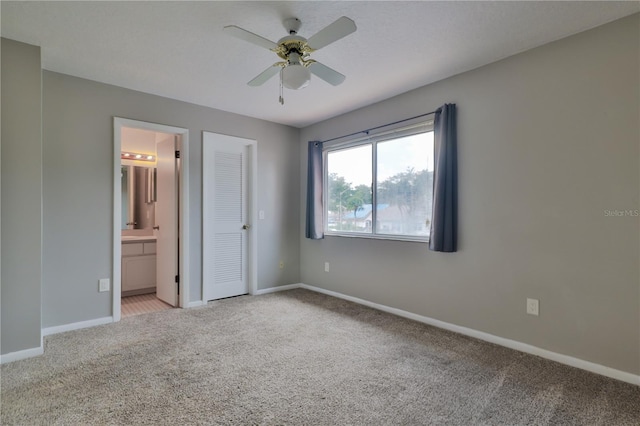 unfurnished bedroom featuring light colored carpet, ensuite bath, a closet, and ceiling fan