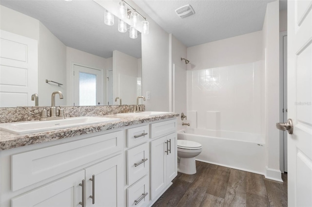 full bathroom with a textured ceiling, wood-type flooring, vanity, shower / bath combination, and toilet