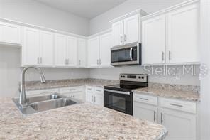 kitchen featuring light stone countertops, sink, white cabinetry, and stainless steel appliances