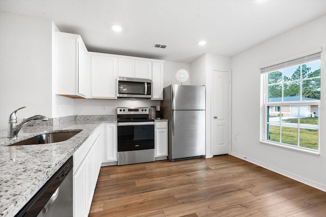 kitchen with sink, stainless steel appliances, light stone counters, hardwood / wood-style floors, and white cabinets