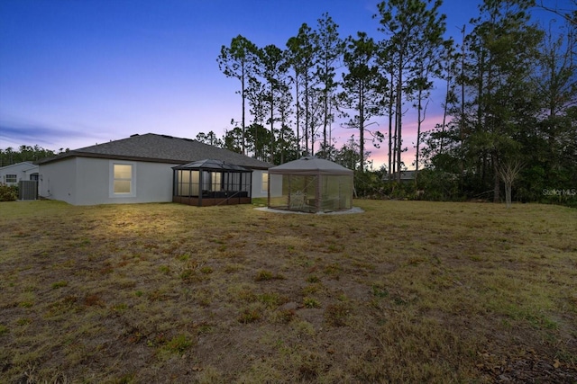 back house at dusk with a lanai and a yard