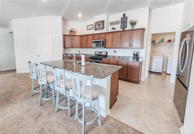 kitchen with washer and clothes dryer, a center island with sink, sink, a breakfast bar area, and stainless steel appliances