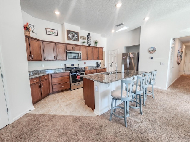 kitchen featuring a kitchen island with sink, light carpet, stainless steel appliances, and a textured ceiling