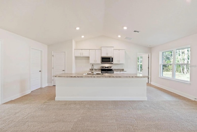 kitchen with light stone countertops, white cabinetry, stainless steel appliances, and an island with sink