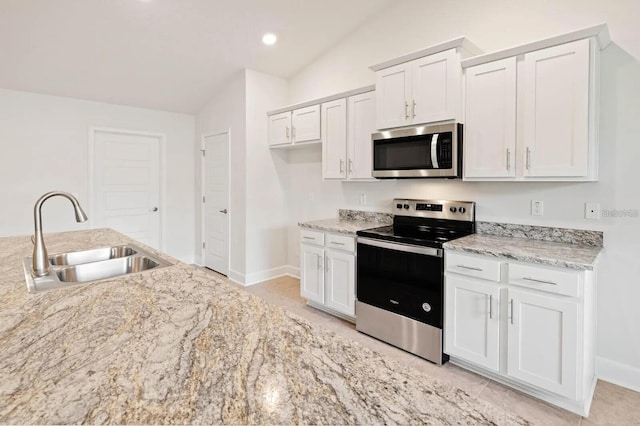 kitchen featuring stainless steel appliances, vaulted ceiling, sink, light tile patterned floors, and white cabinets