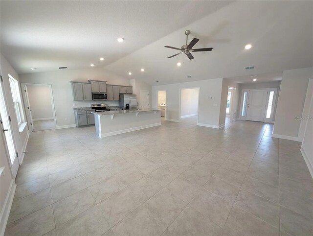 kitchen with gray cabinetry, a wealth of natural light, lofted ceiling, a kitchen island with sink, and appliances with stainless steel finishes