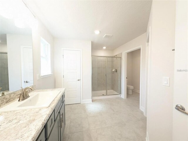 bathroom featuring tile patterned flooring, a textured ceiling, toilet, a shower with door, and vanity