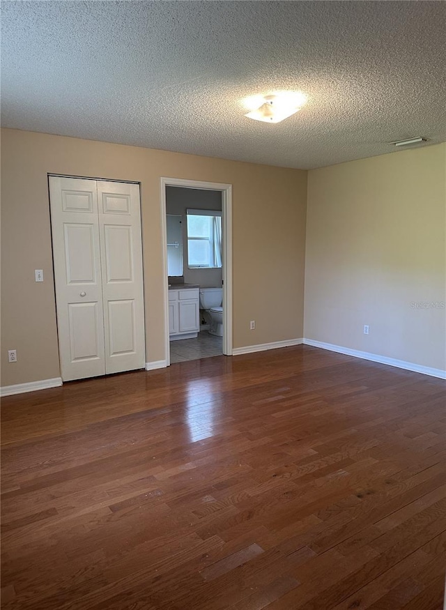 unfurnished bedroom featuring connected bathroom, a closet, dark wood-type flooring, and a textured ceiling