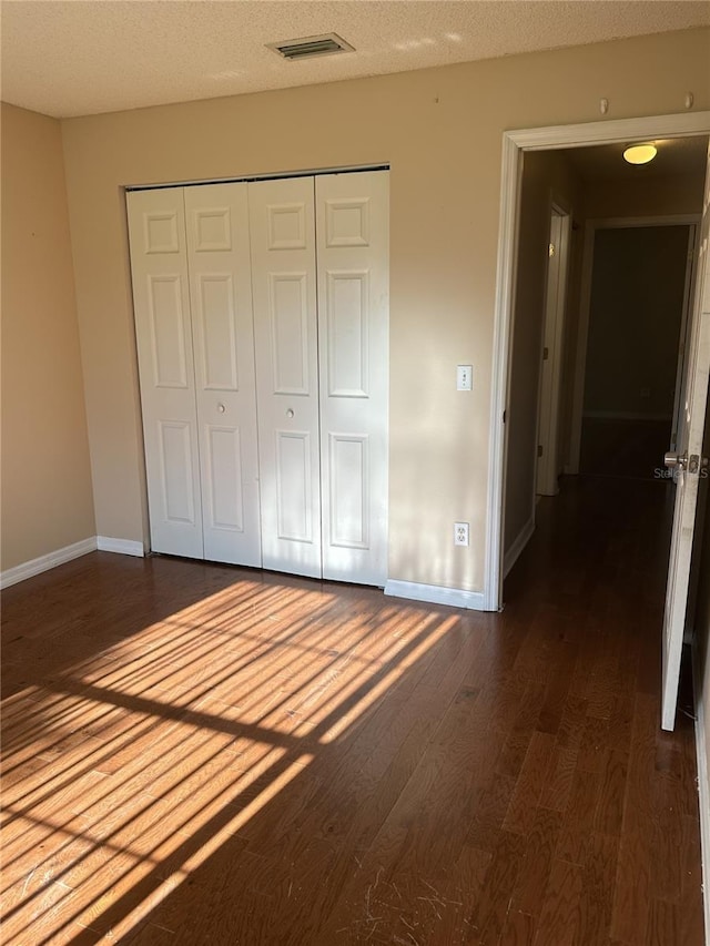 unfurnished bedroom featuring dark hardwood / wood-style flooring, a textured ceiling, and a closet