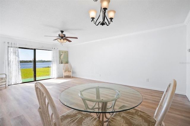 dining space with ornamental molding, a textured ceiling, ceiling fan with notable chandelier, a water view, and hardwood / wood-style flooring