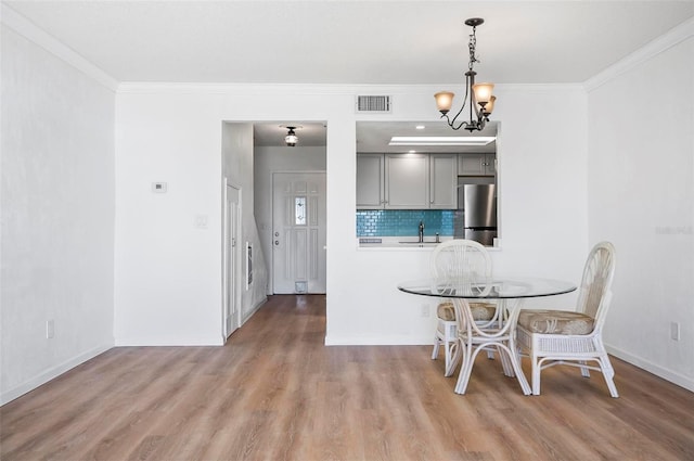 dining area featuring ornamental molding, light hardwood / wood-style floors, a notable chandelier, and sink