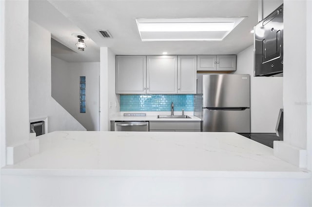 kitchen featuring gray cabinetry, sink, decorative backsplash, light stone countertops, and appliances with stainless steel finishes