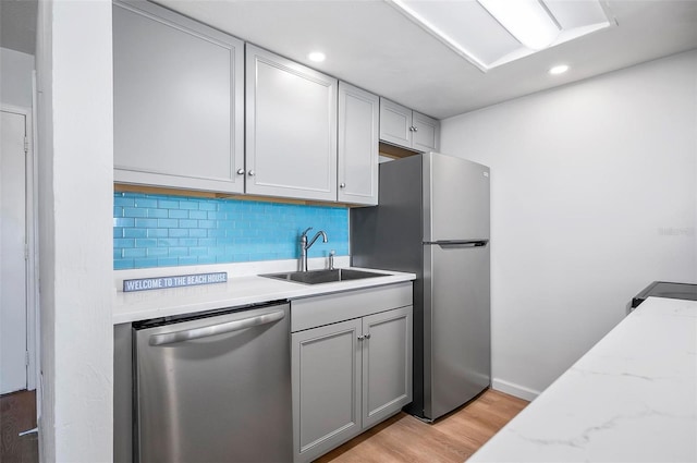 kitchen featuring gray cabinetry, backsplash, sink, light wood-type flooring, and stainless steel appliances