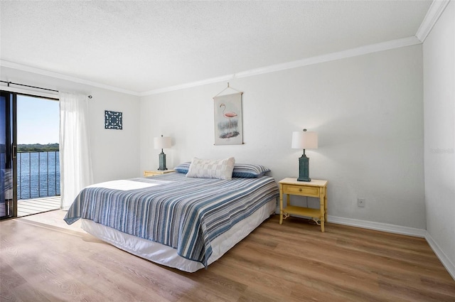 bedroom with crown molding, hardwood / wood-style floors, a textured ceiling, access to outside, and a water view