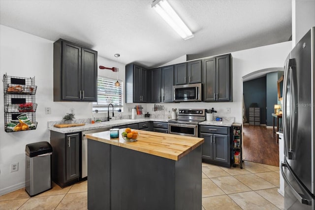 kitchen featuring sink, stainless steel appliances, wooden counters, lofted ceiling, and light tile patterned floors