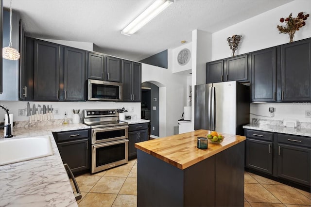 kitchen with appliances with stainless steel finishes, butcher block countertops, vaulted ceiling, and sink