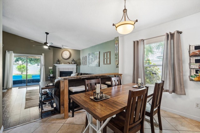 tiled dining space with a tile fireplace, vaulted ceiling, and ceiling fan