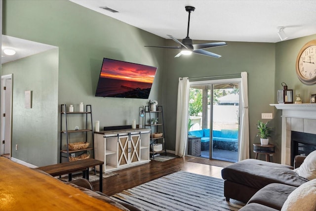 living room with hardwood / wood-style flooring, vaulted ceiling, ceiling fan, and a tiled fireplace