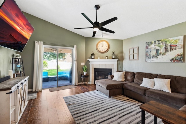 living room with dark hardwood / wood-style floors, ceiling fan, lofted ceiling, and a tiled fireplace