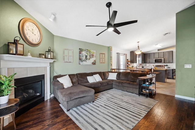 living room with dark hardwood / wood-style floors, ceiling fan, a fireplace, and vaulted ceiling