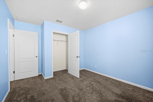 unfurnished bedroom featuring a textured ceiling, dark carpet, and a closet