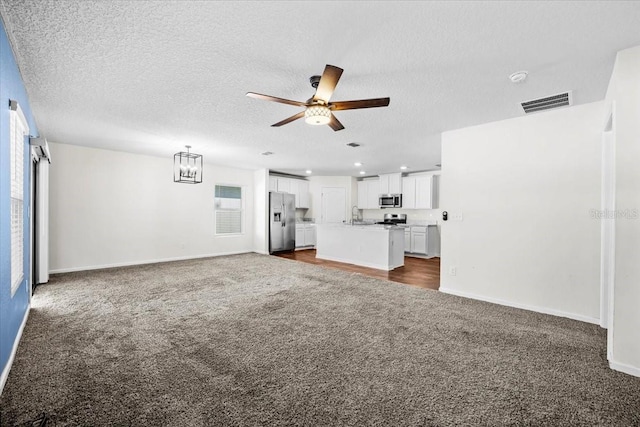 unfurnished living room featuring sink, dark carpet, a textured ceiling, and ceiling fan