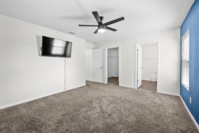 unfurnished bedroom with connected bathroom, dark colored carpet, a walk in closet, ceiling fan, and a textured ceiling