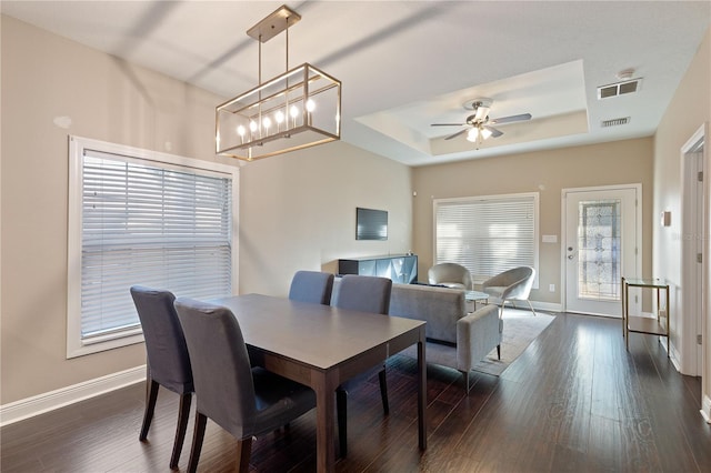 dining area featuring ceiling fan with notable chandelier, dark wood-type flooring, and a tray ceiling