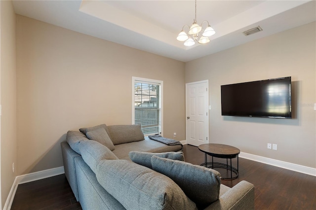 living room featuring a tray ceiling, dark hardwood / wood-style flooring, and an inviting chandelier