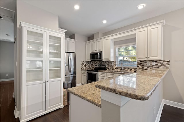 kitchen featuring kitchen peninsula, appliances with stainless steel finishes, tasteful backsplash, sink, and white cabinetry