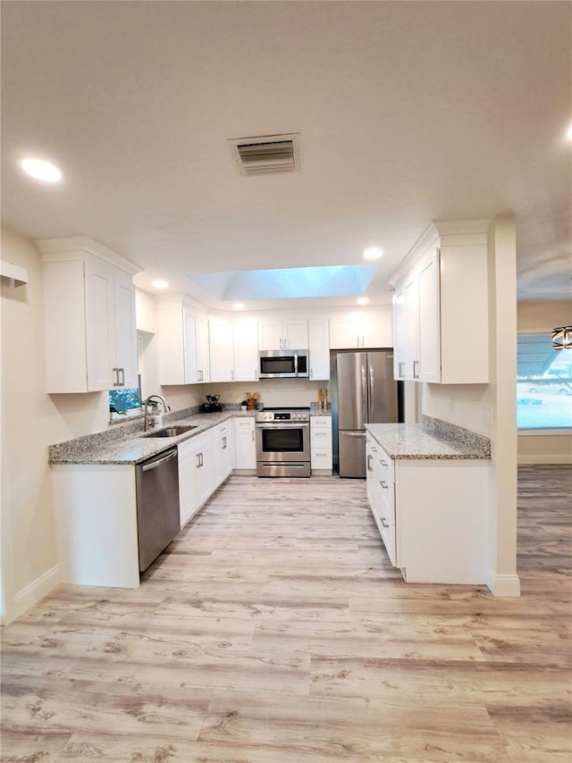 kitchen featuring light stone countertops, appliances with stainless steel finishes, sink, light hardwood / wood-style floors, and white cabinetry