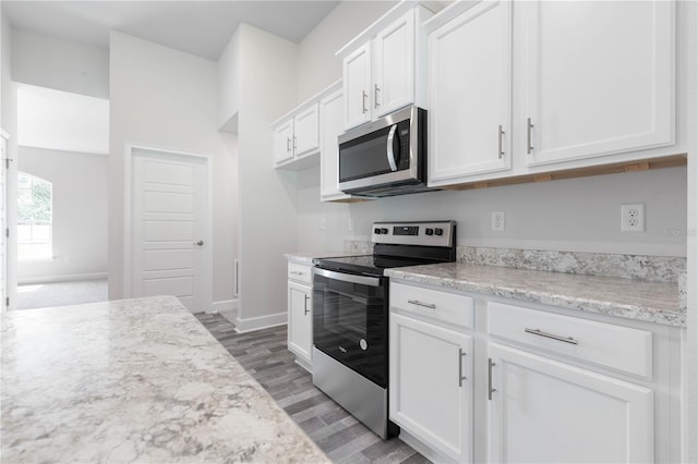 kitchen with hardwood / wood-style floors, light stone countertops, white cabinetry, and appliances with stainless steel finishes