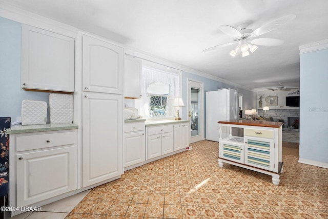 kitchen featuring ornamental molding, ceiling fan, light tile patterned floors, white fridge, and white cabinetry