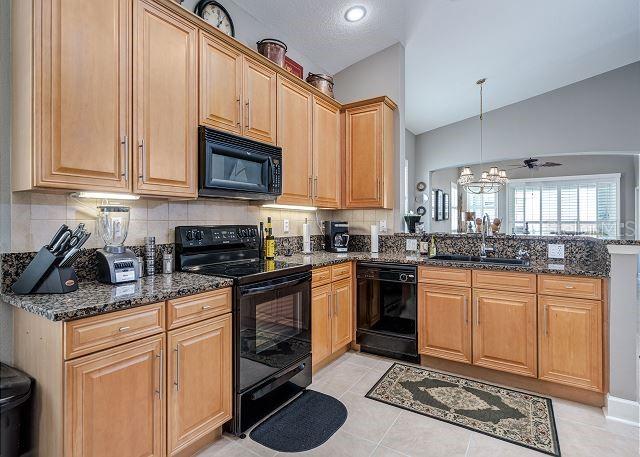 kitchen with sink, hanging light fixtures, dark stone counters, and black appliances