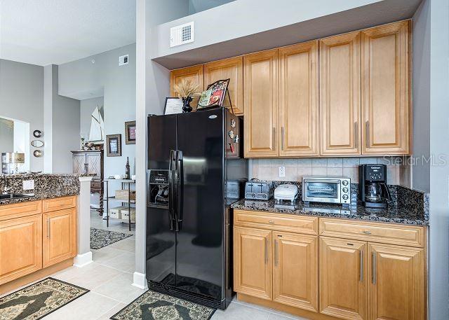 kitchen featuring decorative backsplash, dark stone countertops, light tile patterned floors, and black refrigerator with ice dispenser