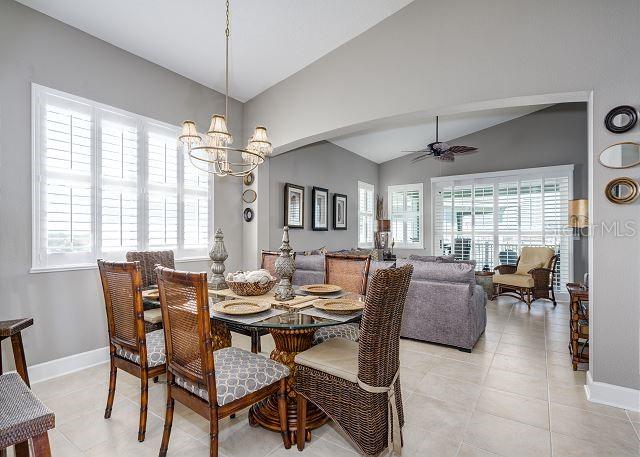 dining space featuring light tile patterned floors, ceiling fan with notable chandelier, vaulted ceiling, and a wealth of natural light